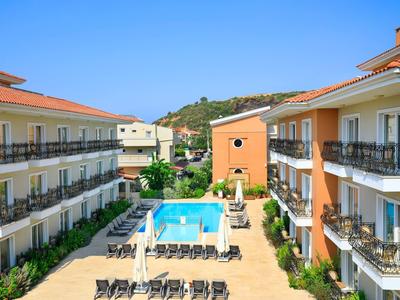 Hotel mit Poolzone in der Mitte, zwei Gebäudeflügel mit Balkonen, blauem Himmel und grüner Umgebung.