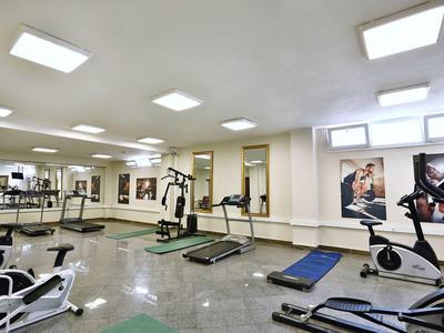 Großer Fitnessraum mit diversen Trainingsgeräten, Spiegeln und hellen Deckenlampen.