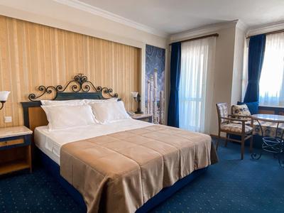 Helles Schlafzimmer mit großem Bett, beige Decke, Holzvertäfelung und blauem Teppichboden.