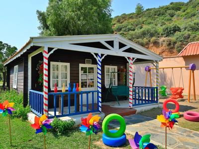 Buntes Ferienhaus mit Veranda, umgeben von grüner Wiese, Hügeln und farbigen Windrädern.