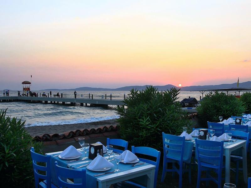 Evening view of set restaurant tables by the sea with sunset in the background.