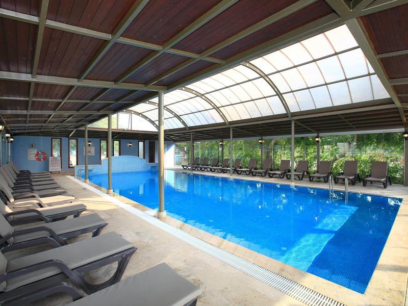 Indoor pool with lounge chairs and large windows overlooking greenery.