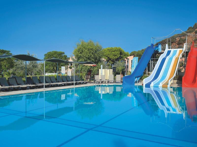 Large pool with colorful water slides and umbrellas in the hotel garden under clear sky.