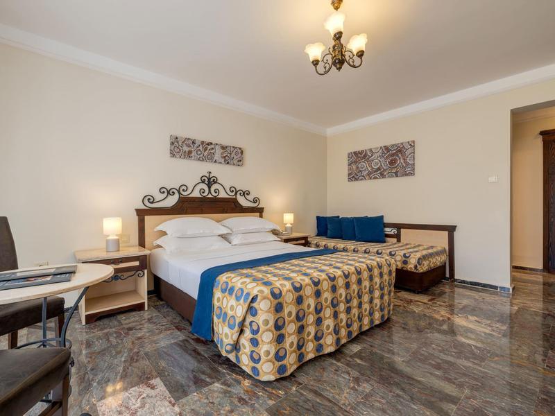 Elegant hotel room with double bed, nightstands, chairs, and decorative wall art.