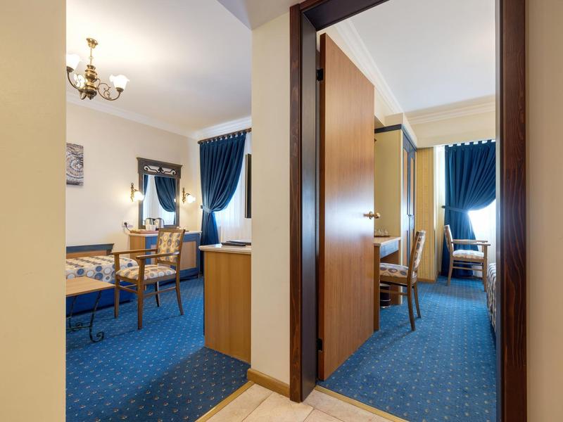 View through open doors into two rooms with blue curtains and carpet flooring in a hotel.