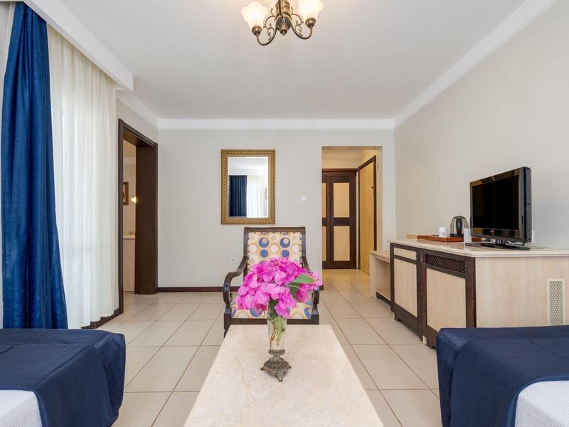 Bright hotel room with two beds, a bouquet on the table, and a TV on the cabinet.