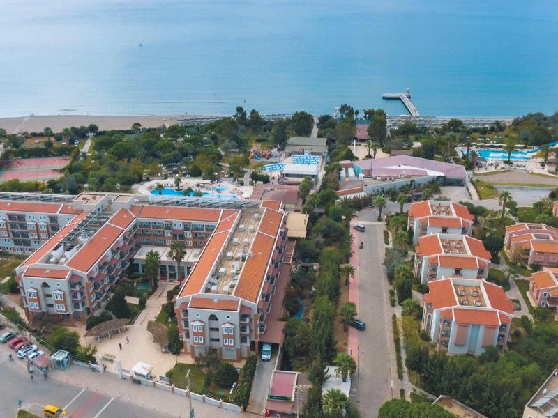 Aerial view of a hotel complex with residential buildings, pools, and sea view in the background.