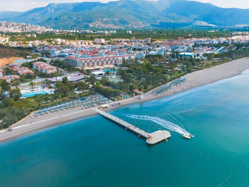 Aerial view of a long pier extending into the calm blue sea in front of a coastal town.
