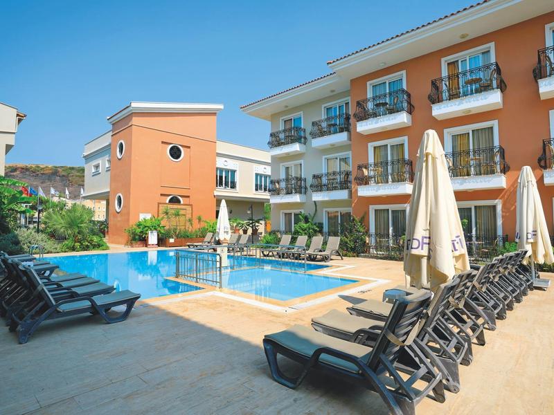 Modern outdoor pool area with loungers and umbrellas in front of a hotel building.
