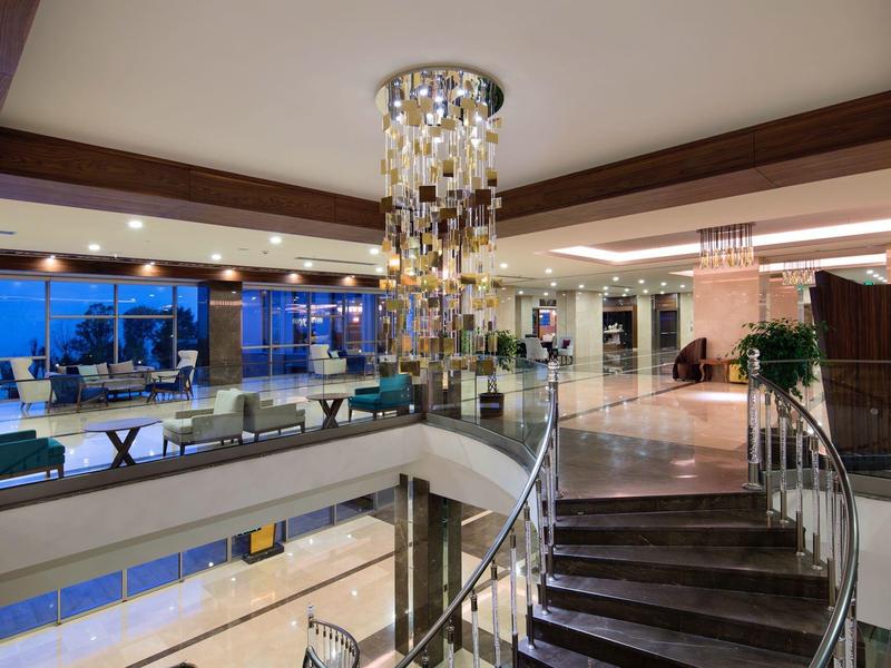 Area lobby moderna dell'hotel con grande lampadario di cristallo e scala a chiocciola alla luce serale.