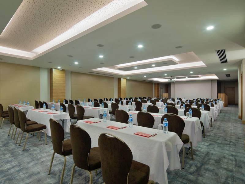 Sala conferenze moderna con tovaglie bianche e file di sedie.