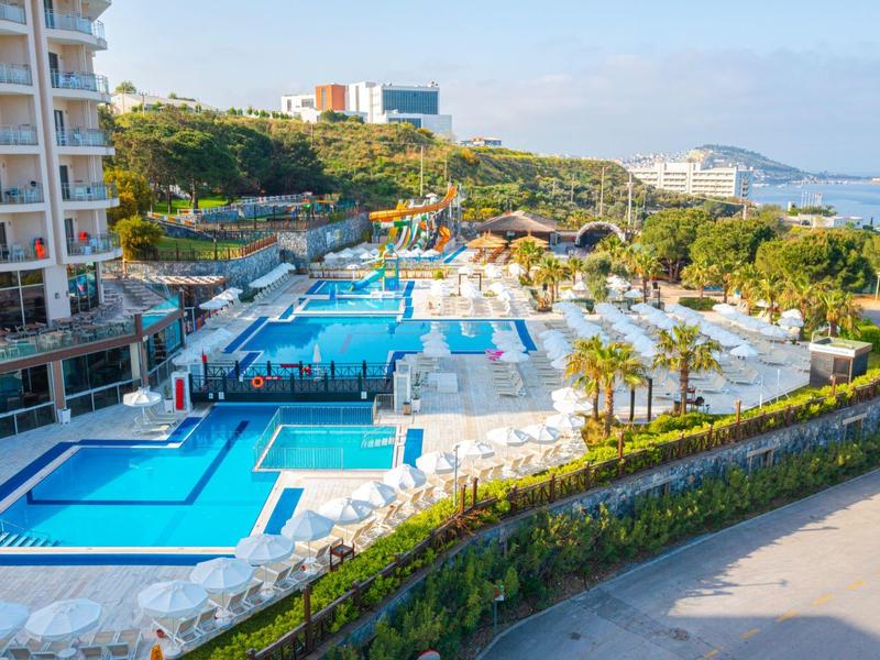 Hotel moderno con più piscine e lettini, circondato da verde e vista mare.