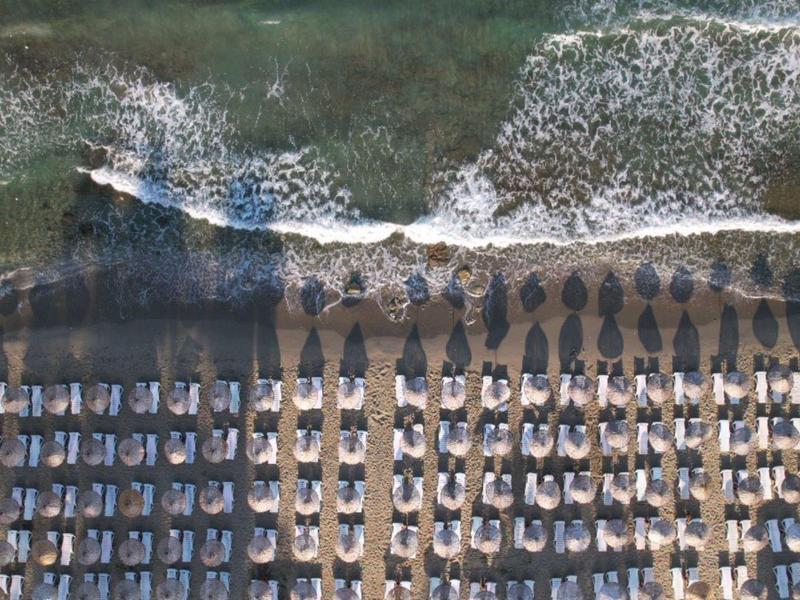 Vista aerea di una spiaggia con ombrelloni e lettini accanto al mare.