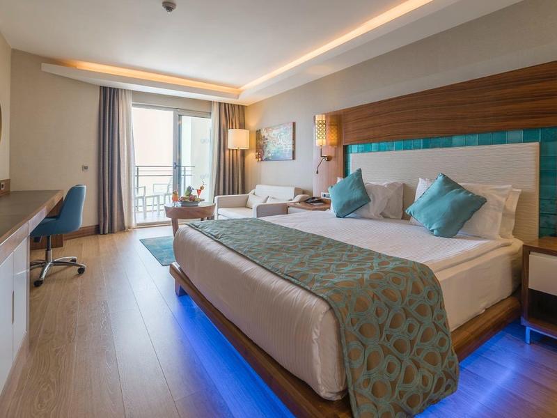 Camera d'hotel moderna con letto grande, illuminazione ambientale blu e balcone con vista mare.