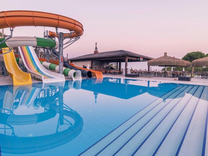 Grande piscina con scivoli d'acqua e ombrelloni al tramonto.