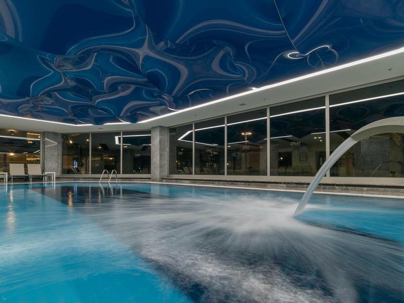 Piscina interna moderna con getti d'acqua e volta del soffitto blu artisticamente progettata.