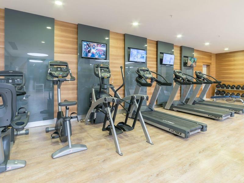 Palestra moderna con macchine cardio e pesi in uno spazio luminoso e aperto.