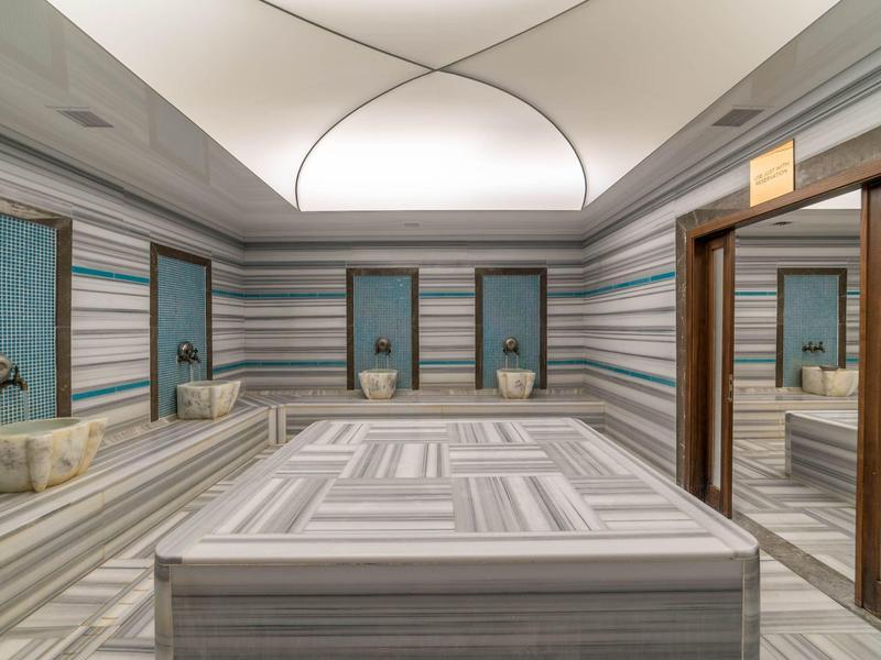 Area spa moderna dell'hotel con grande piscina termale centrale e pareti a piastrelle rigate.