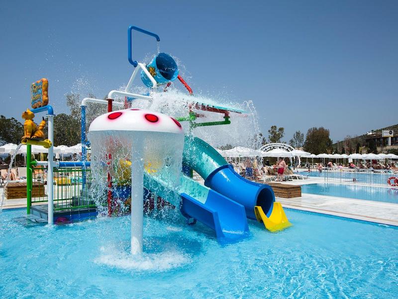 Parco giochi acquatico colorato con scivoli e doccia d'acqua in una piscina di un hotel sotto il sole.