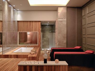 Camera d'hotel moderna con dettagli in legno, due poltrone rosse e un ampio bagno con vasca da bagno.