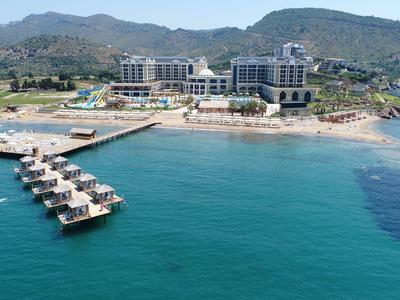Hotelanlage am Küstenhang mit langen Stegen und glasklarem blauem Wasser, umgeben von grünen Hügeln.