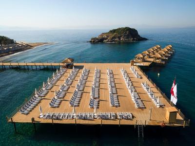 Große Holzplattform mit Liegestühlen und Sonnenschirmen über blauem Meer und kleinem Inselchen.