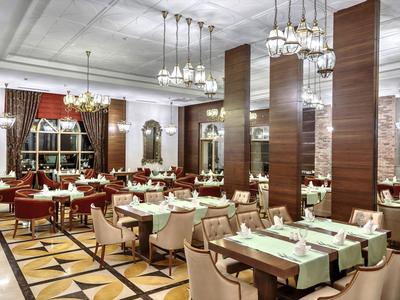 Großes Restaurant mit weißen Tischen, roten und beige Sesseln, Holzsäulen und Kronleuchtern.