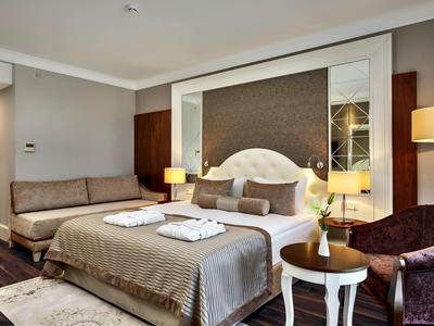 Modern eingerichtetes Schlafzimmer mit Doppelbett, Sofa, Sessel und warmem Lichtakzent.