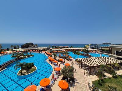 Großer Hotelpool mit blauer Wasserfläche, orangefarbenen Liegestühlen und Blick auf das Meer.