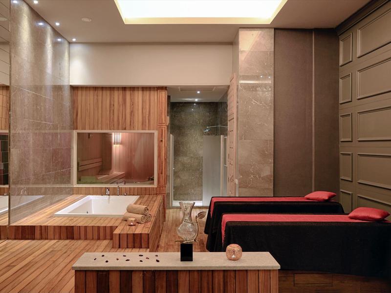 Moderner Wellnessraum mit Holzakzenten, rotem Sofa, Whirlpool und Glasdusche in warmem Licht.