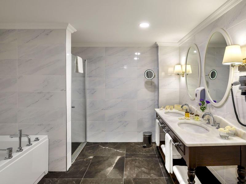 Modernes Badezimmer mit Marmorwänden, Doppelwaschbecken, großer Dusche und eingebauter Badewanne.