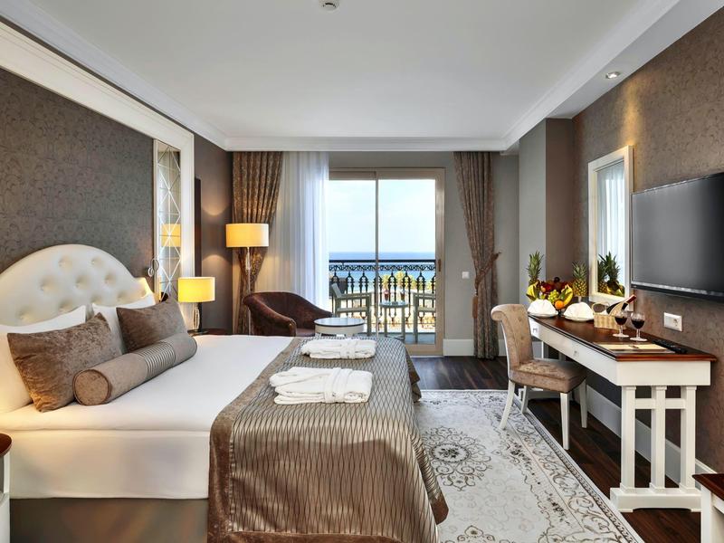 Modernes Hotelzimmer mit großem Bett, Schreibtisch, Fernseher und Balkon mit Meerblick.