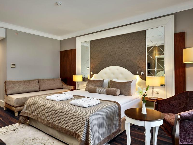 Modern eingerichtetes Schlafzimmer mit Doppelbett, Sofa, Sessel und warmem Lichtakzent.