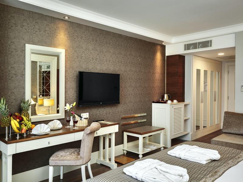 Helles Hotelzimmer mit Doppelbett, Fernseher, Schreibtisch, Stuhl und dekorativer Wandgestaltung.