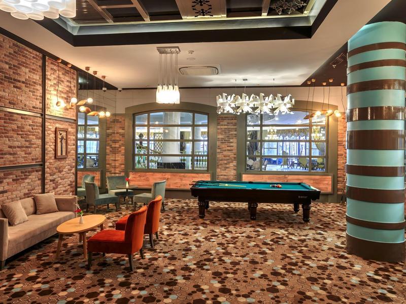 Gemütlicher Spielebereich mit Billardtisch, Sofa, bunten Sesseln und dekorativer Säule in warmem Licht.