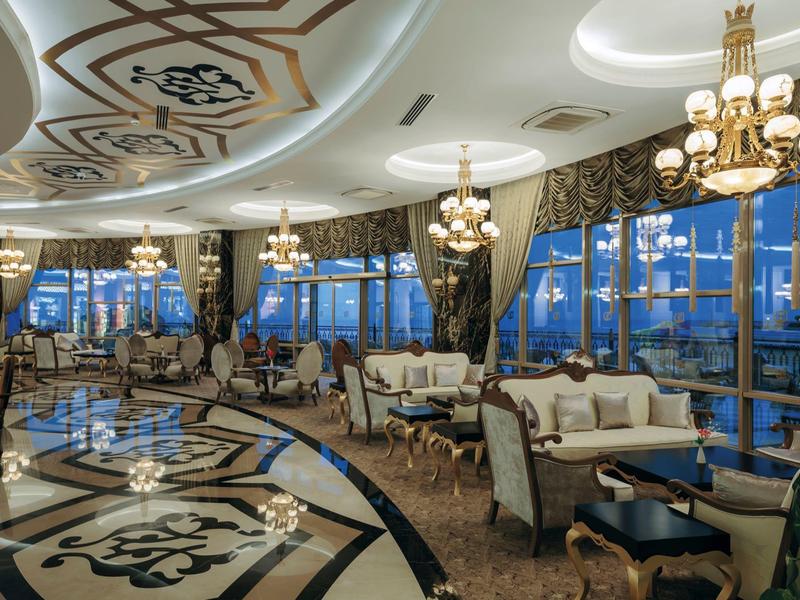 Luxuriöser Saal mit großen Fenstern, Kronleuchtern und eleganter weiß-beiger Einrichtung.