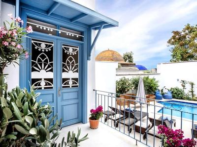 Terrasse mit blauen Türen, weißen Wänden, bunten Blumen und blauem Swimmingpool.