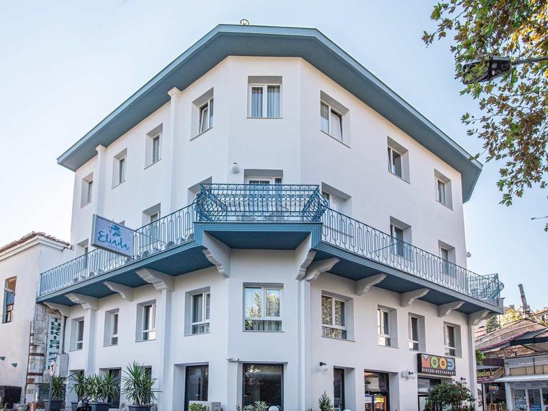 Modernes dreistöckiges weißes Eckgebäude mit blauen Balkonen und Fenstern, umgeben von Bäumen.