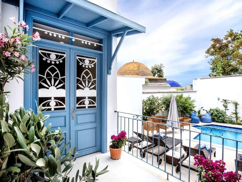 Terrasse mit blauen Türen, weißen Wänden, bunten Blumen und blauem Swimmingpool.