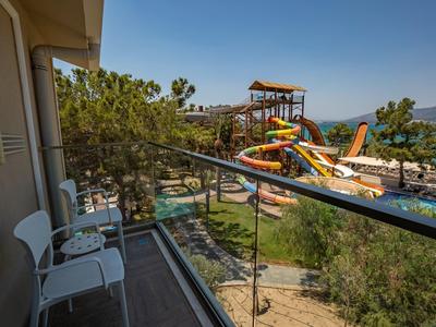 Balkon mit zwei weißen Stühlen und Blick auf bunten Wasserpark mit Rutschen und Bäumen.