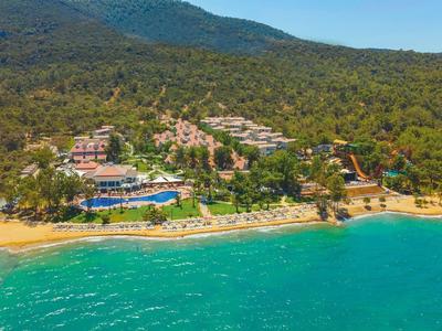 Küste mit türkisfarbenem Meer, Sandstrand, Hotels und Wald im Hintergrund, Berge am Horizont.