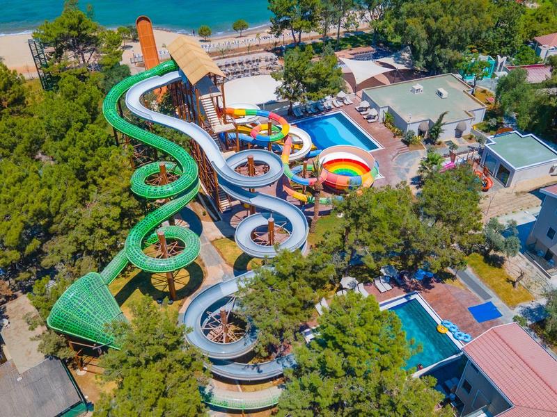 Bunter Wasserpark mit mehreren Rutschen, umgeben von Bäumen und Gebäuden nahe einem Strand.