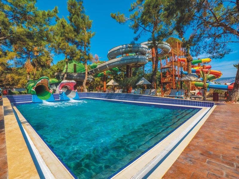Buntes Wasserpark mit blauen Pool, Rutschen und umgeben von grünem Pinienwald unter klarem Himmel.