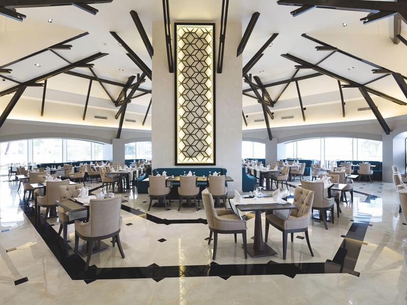 Helles, modernes Restaurant mit hohen Decken, vielen Tischen und eleganten Stühlen in hellem Holz.