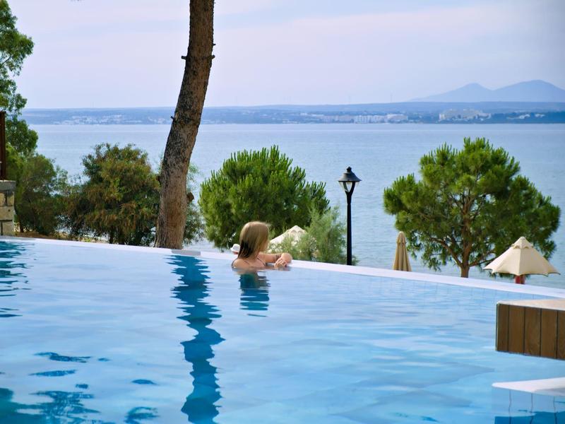 Ein Mann entspannt im Infinity-Pool mit Blick auf Meer und Bäume am hellen Tag.