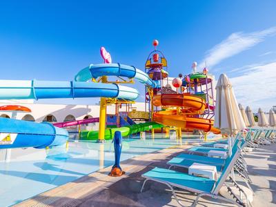 Bunter Wasserpark mit mehreren Rutschen und Liegestühlen unter blauem Himmel.