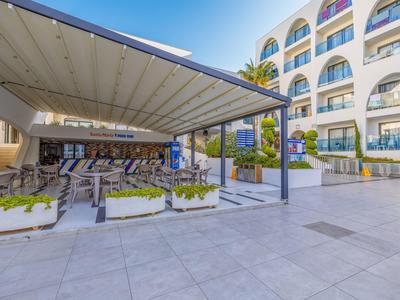 Moderner Hotelbereich mit überdachter Terrasse und Sitzgelegenheiten vor einem weißen Gebäude.