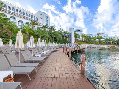 Hotelterrasse mit Liegestühlen, Sonnenschirmen und Blick auf das Meer unter blauem Himmel.
