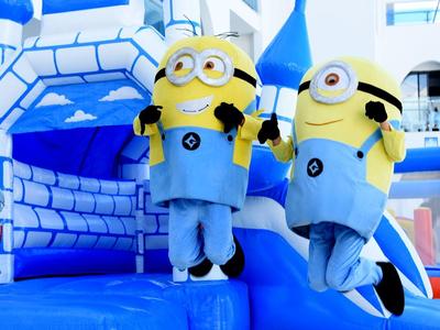 Zwei Personen in Minion-Kostümen springen auf einer blauen Hüpfburg mit Burg-Design.