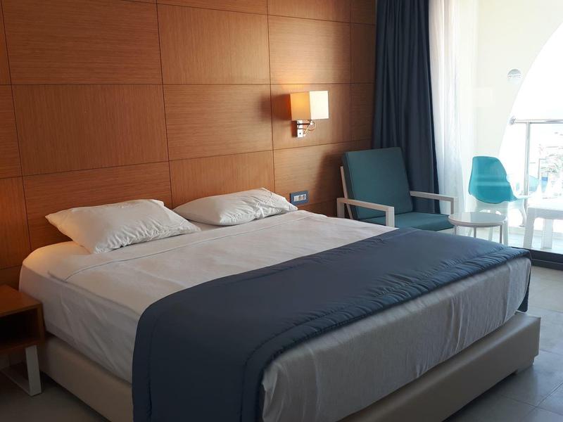 Modernes Hotelzimmer mit Doppelbett, Holzwand, zwei Sesseln und Balkon mit blauem Vorhang